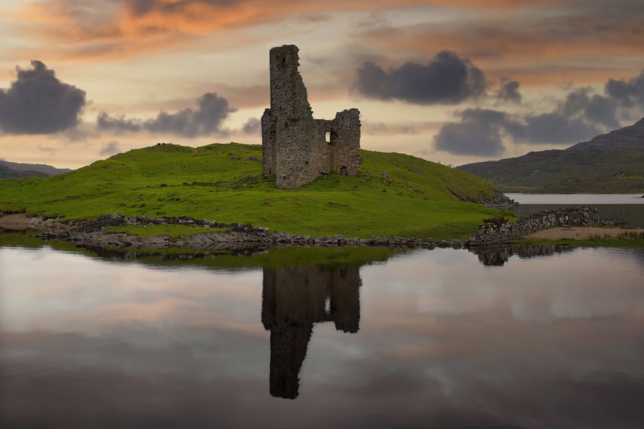Ardvreck Castle reflected in Loch Assynt during a vibrant sunset in Scotland.