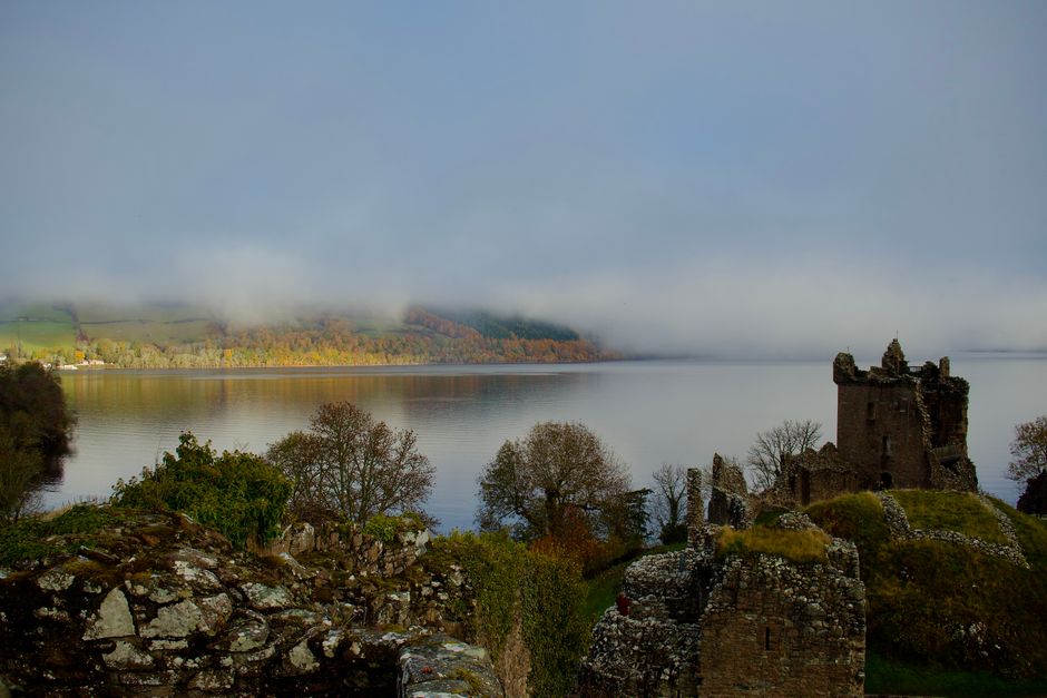 Explore the misty beauty of Urquhart Castle on the serene shore of Loch Ness in Scotland, a perfect autumn scene.
