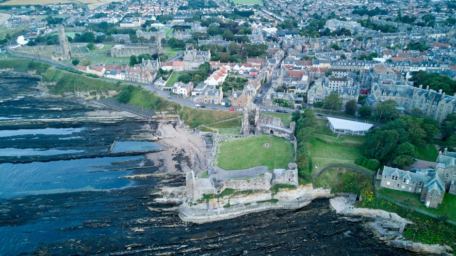 Drone shot of St Andrews Castle and coastal city in Fife, Scotland, showcasing historical architecture and scenic seashore.