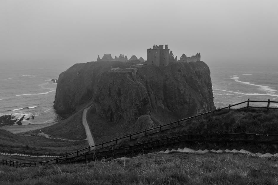 Atmospheric black and white photo of Dunnottar Castle on a misty coastal cliff.