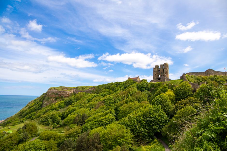 A scenic view of Scarborough Castle ruins with lush greenery and ocean backdrop.